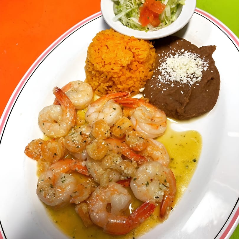 El Don Quijote's Mexican shrimp dish with rice, refried beans, and a side salad.