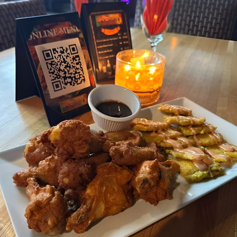 A plate of fried chicken and plantains with sauce, a QR code menu, and a candle.