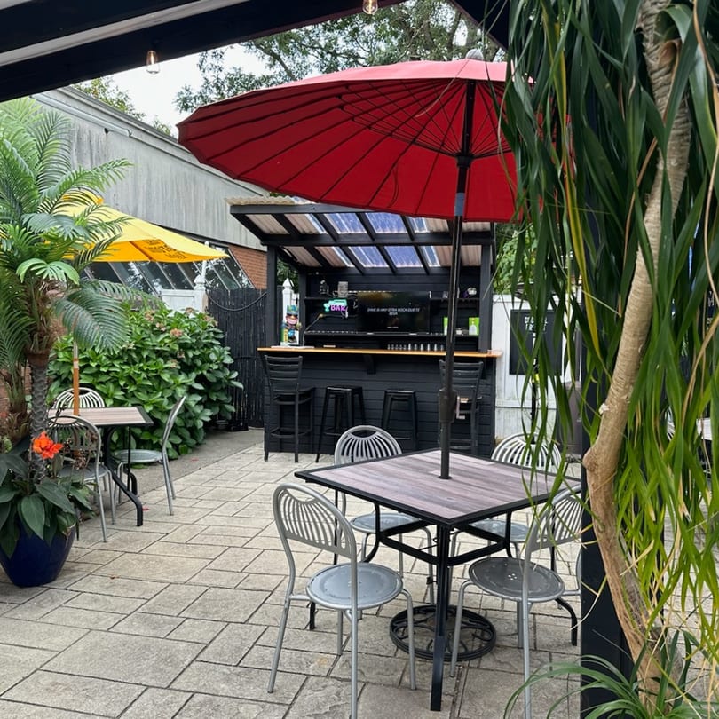 Outdoor patio at El Don Quijote with tables, chairs, a black bar, and red and yellow umbrellas.